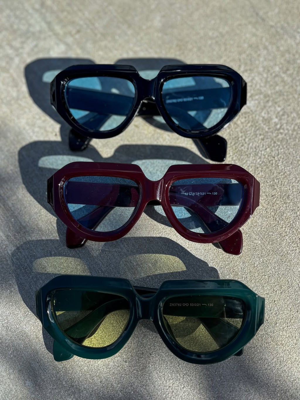 Three pairs of sunglasses with different colored lenses on a textured surface.