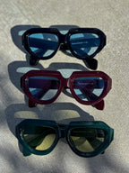Three pairs of sunglasses with different colored lenses on a textured surface.